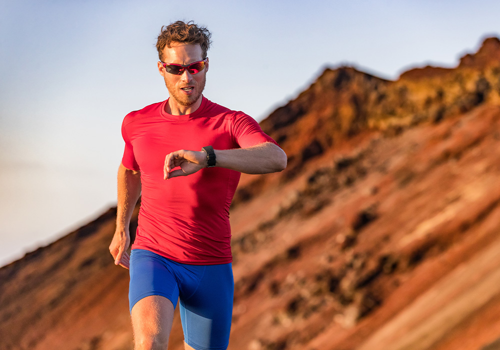 homme qui fait un trail en regardant sa montre connecté avec des lunettes de soleil
